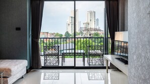 Una moderna camera d'albergo con un balcone, un divano, una TV e vista su edifici alti.
