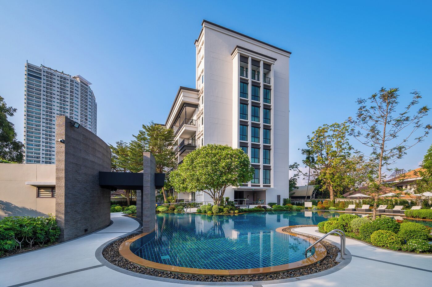 Un hotel moderno con piscina, un edificio alto e rigogliosa vegetazione.