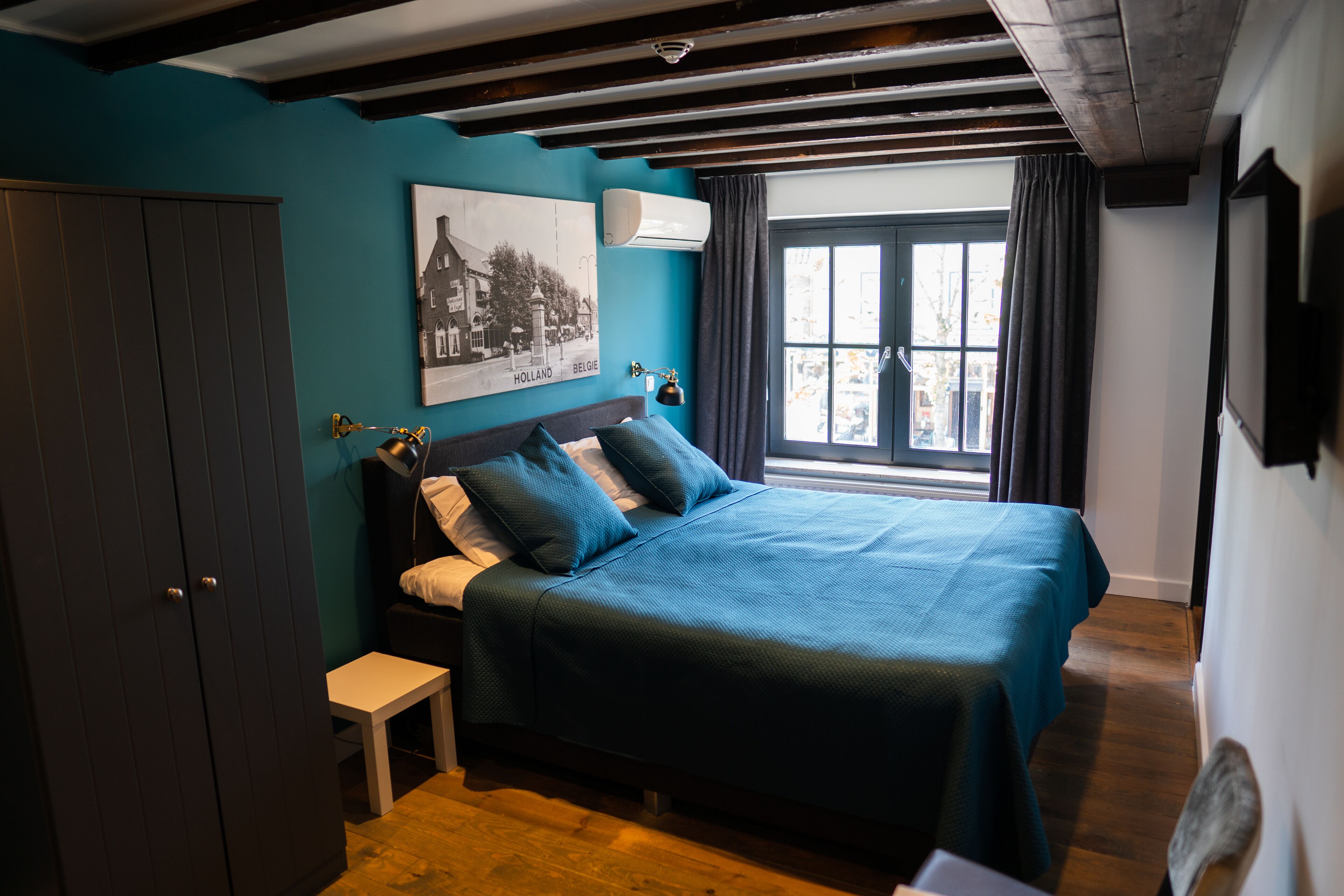 A bedroom with a bed, a nightstand, a wardrobe, a window with curtains, and a wall-mounted air conditioner.