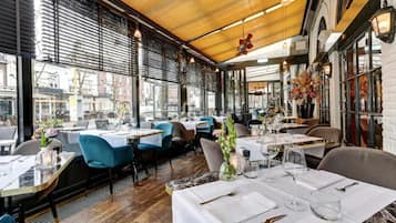 An indoor dining area with tables set for service, large windows, and a wooden ceiling.