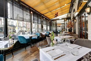 An indoor dining area with tables set for service, large windows, and a wooden ceiling.