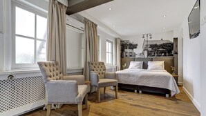 Un dormitorio moderno con una cama grande, dos sillones, un radiador y vistas a un paisaje urbano a través de la ventana.