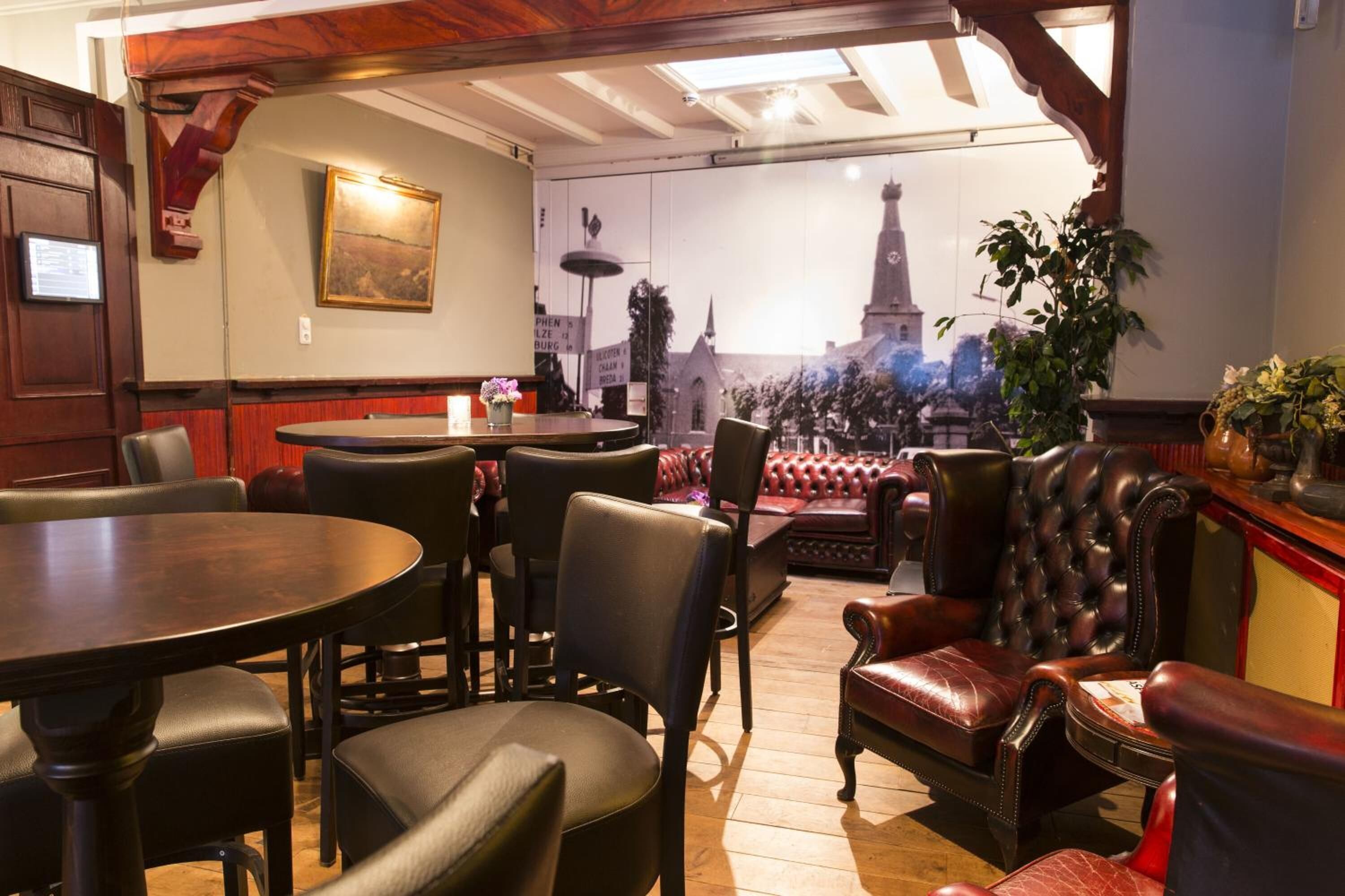 A cozy interior with leather seating, a round table, and a view of a cityscape through a large window.