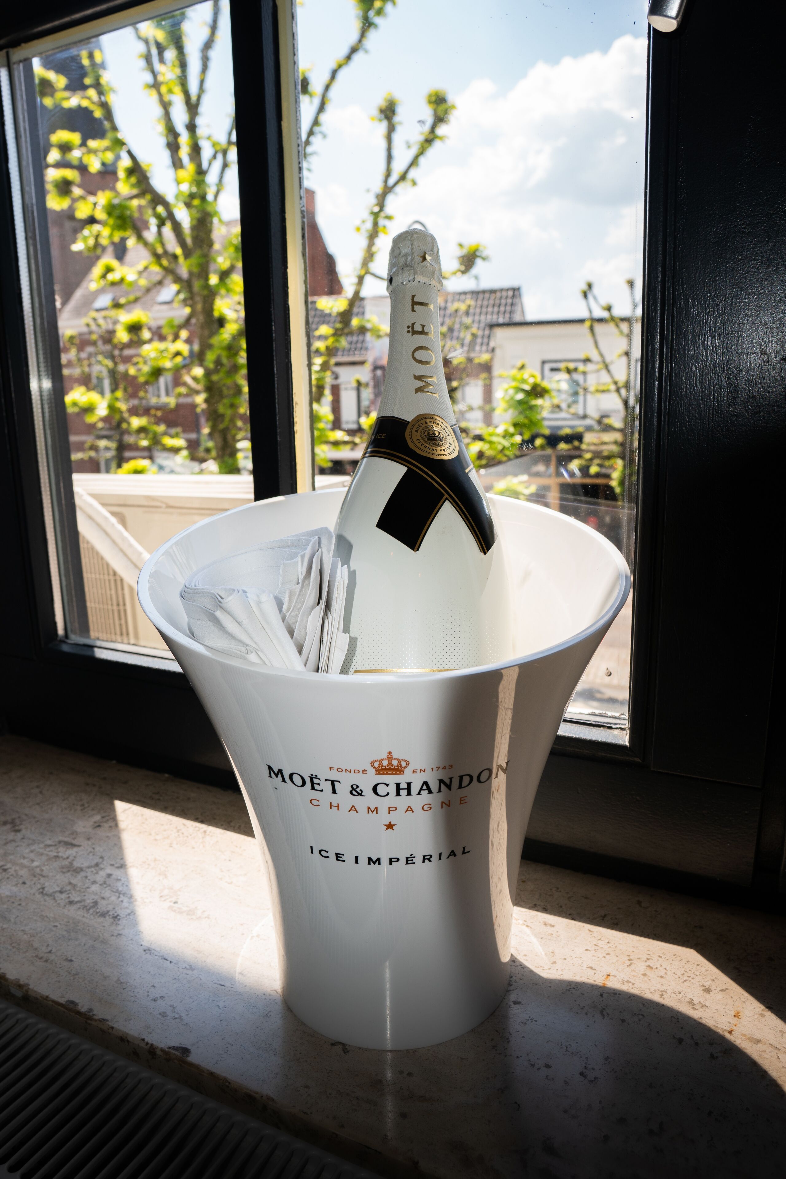 A Moët & Chandon champagne bottle in a white ice bucket on a windowsill.