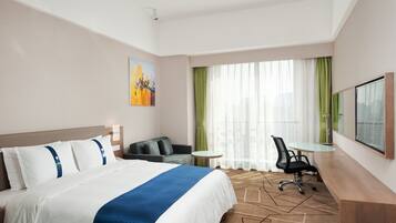A hotel room with a bed, a desk, a chair, a small table, and a large window with curtains.