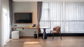 A modern hotel room with a large flat-screen TV, a small refrigerator, a round table, and a comfortable chair. - Holiday Inn Express Chengdu West Gate by IHG (Chengdu)
