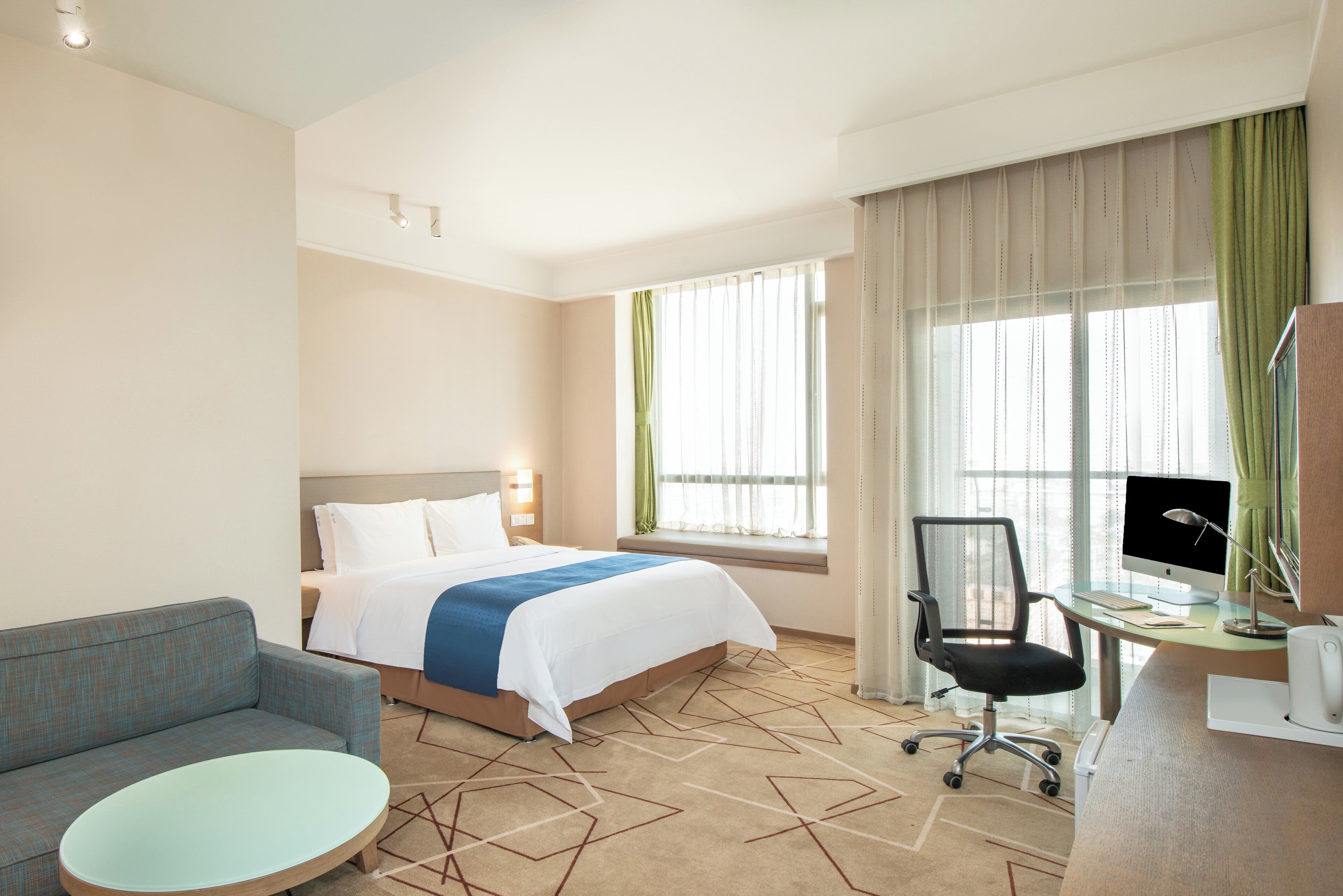 Una habitación de hotel con una cama, un escritorio con computadora, una silla y una mesa redonda.