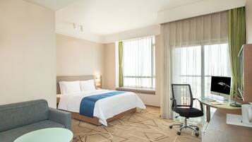 Una habitación de hotel con una cama, un escritorio con computadora, una silla y una mesa redonda.