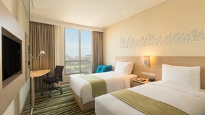Une chambre d’hôtel avec deux lits, un bureau, une chaise, une télévision et une grande fenêtre donnant sur la ville.