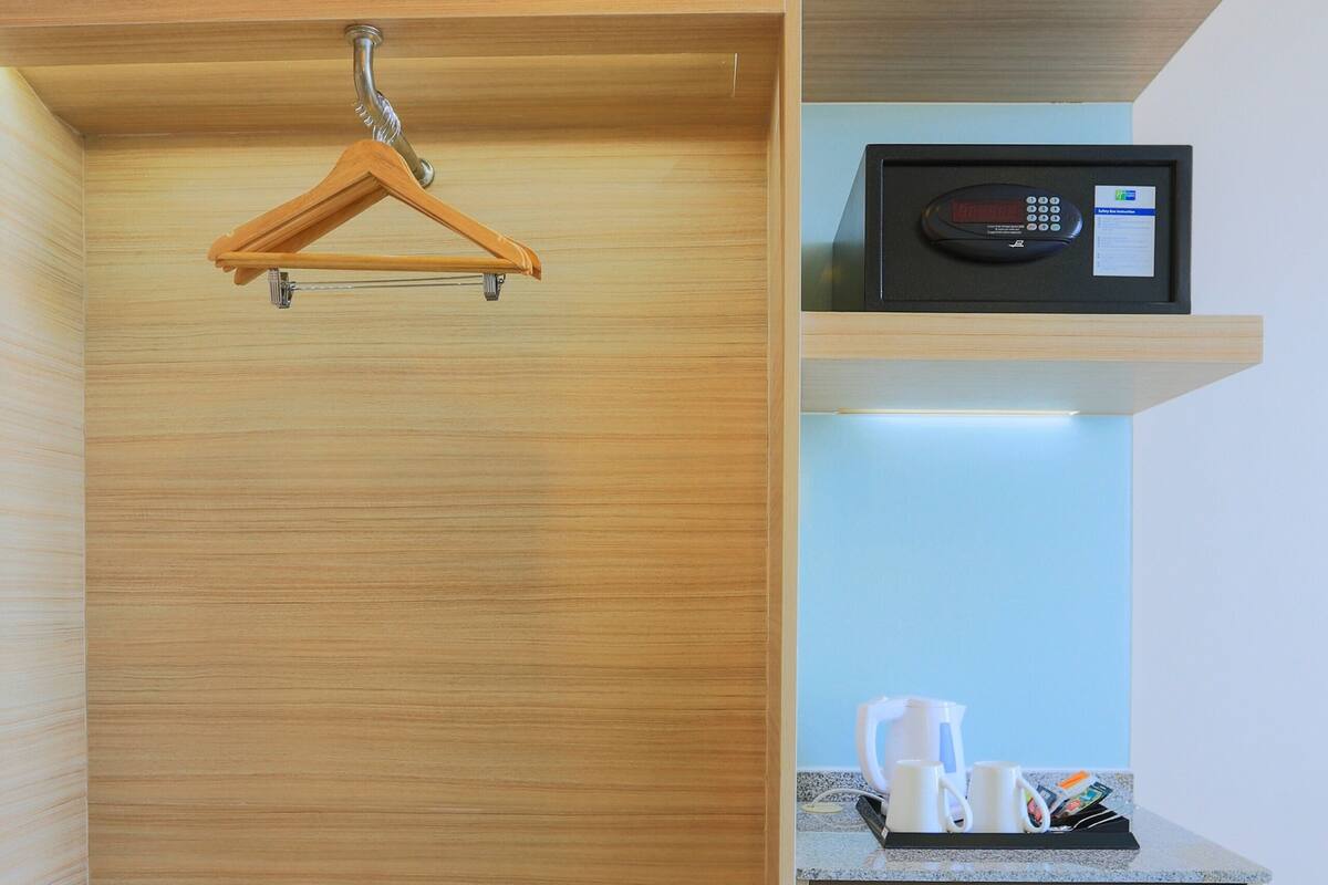 A modern room with a wooden wardrobe, a small desk with a coffee maker, and a digital clock.