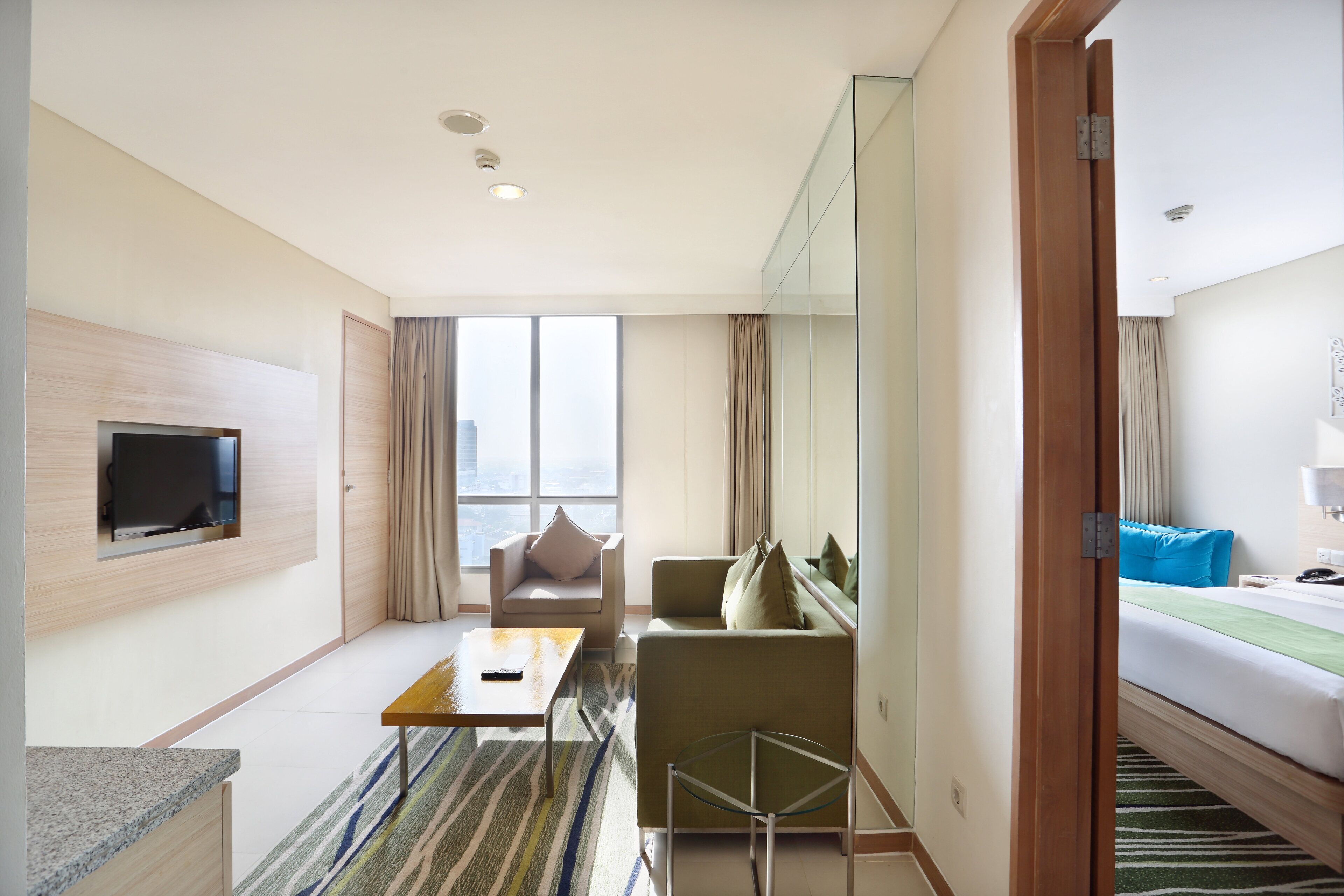 Habitación de hotel moderna con televisión de pantalla plana, un sofá, una cama, una mesita y vistas a la ciudad.