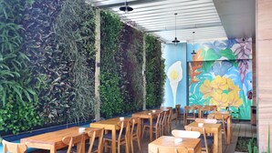 Un espace de restauration intérieur avec des tables et des chaises en bois, un mur végétal vertical et une fresque colorée sur le mur du fond.