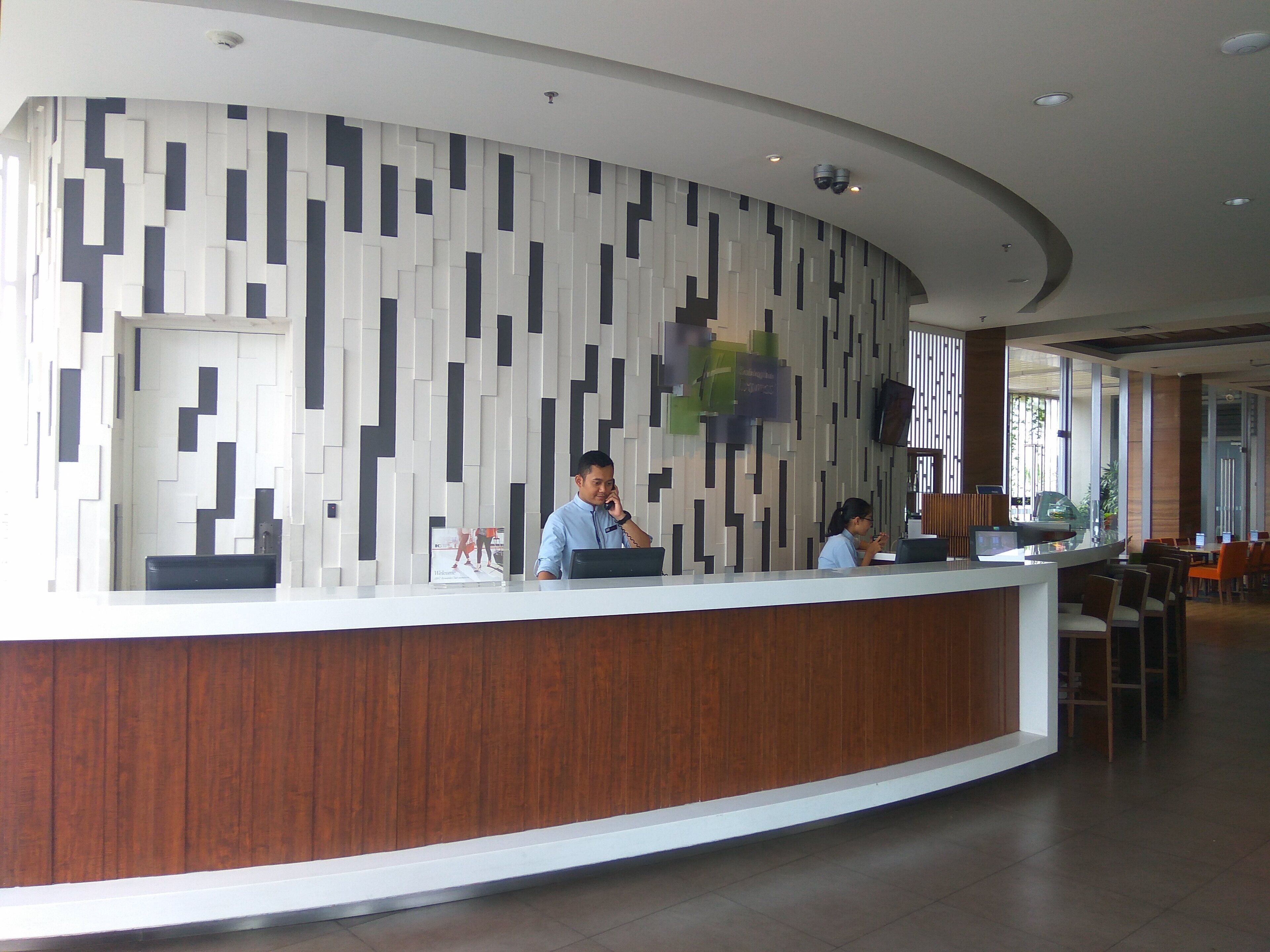 A reception desk with a modern design, two staff members, and a seating area with tables and chairs.