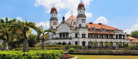 A large, historic building with two prominent towers and a central dome, surrounded by well-maintained gardens and palm trees.