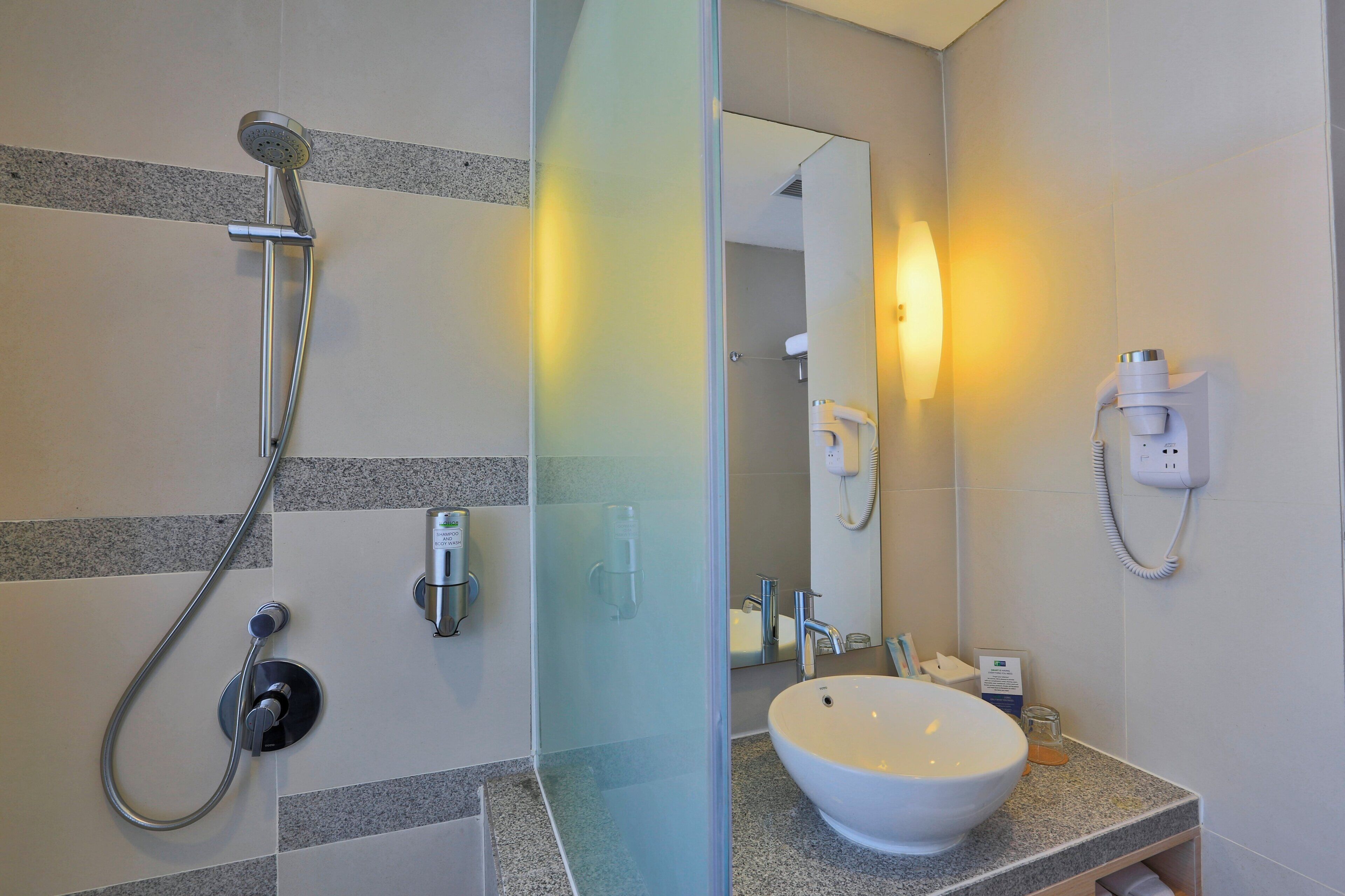 Un bagno con doccia, lavandino, specchio e portasciugamani.