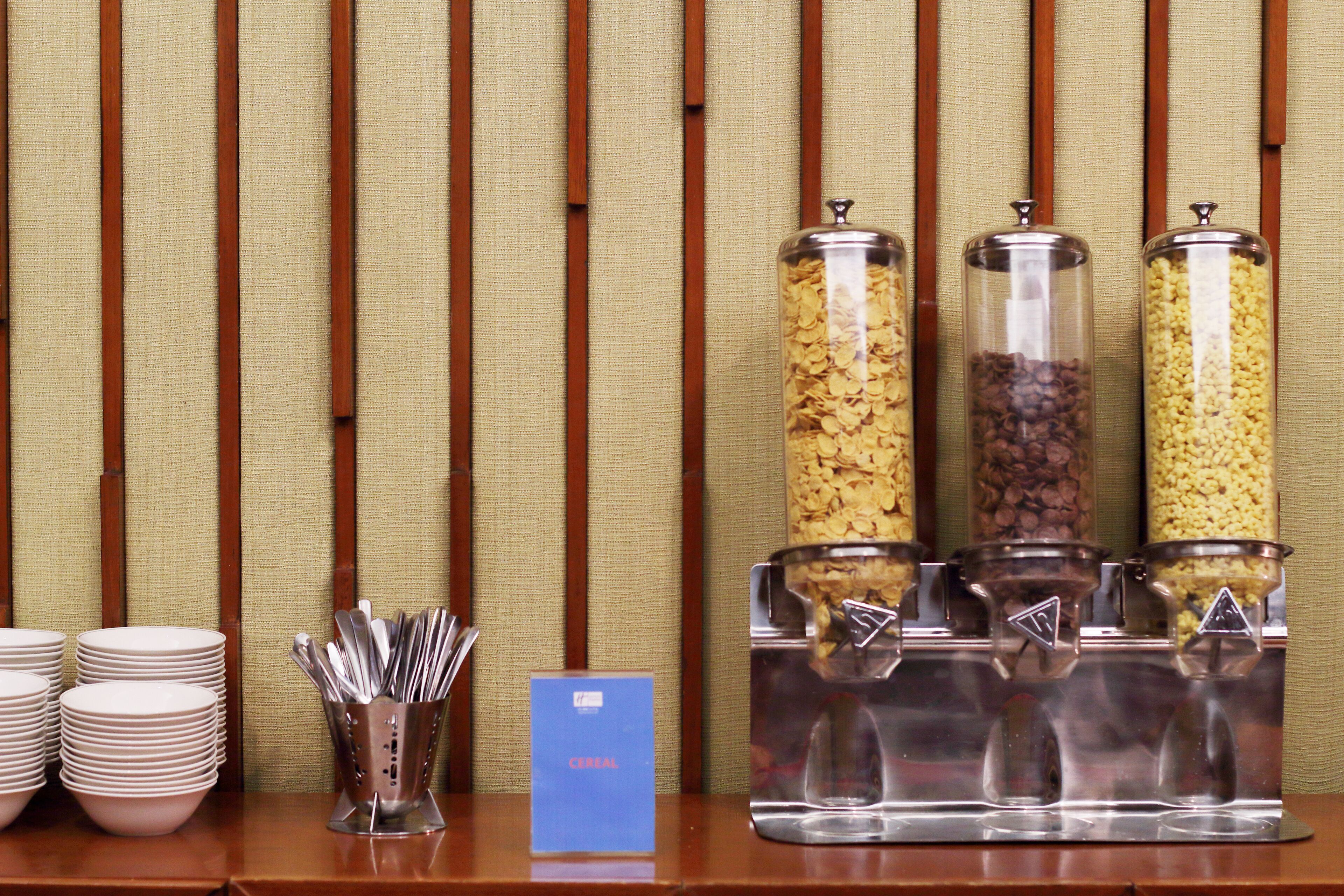 A buffet setup with cereal and coffee dispensers, plates, and utensils.
