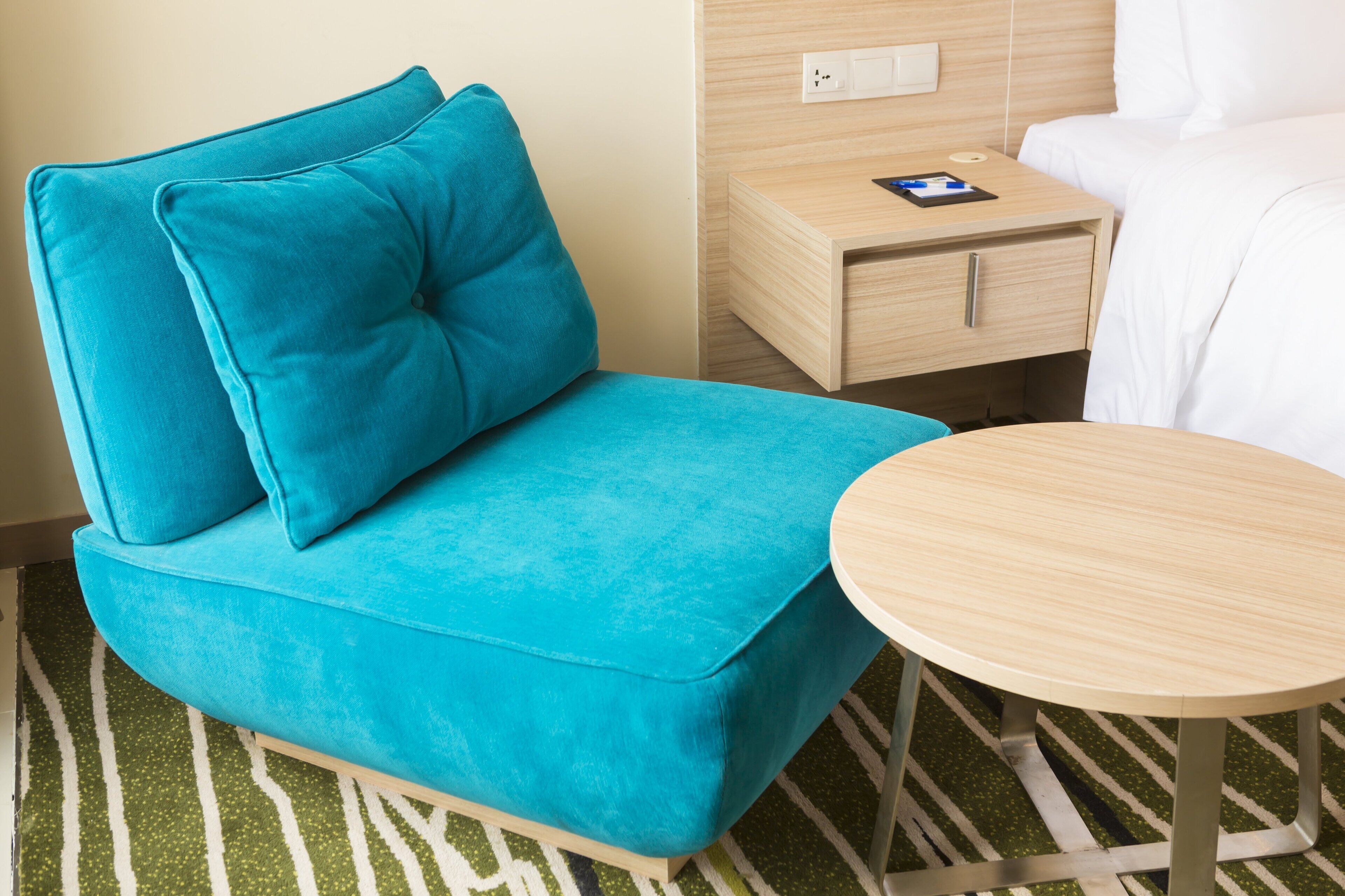 A teal sofa with a matching pillow, a wooden side table with a book, and a round table.