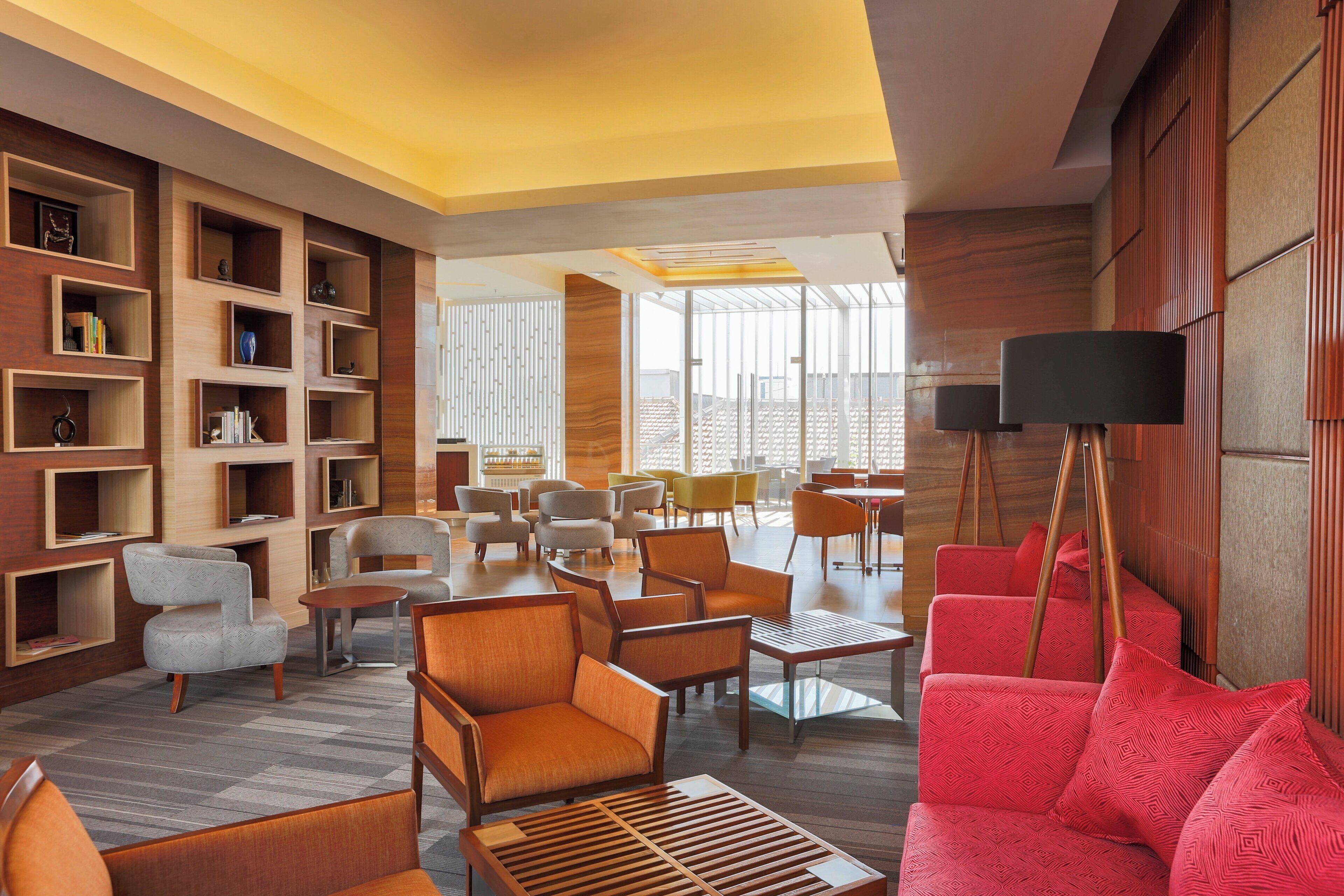 A modern hotel lobby with a variety of seating options, a large window offering a view, and a bookshelf with decorative items.