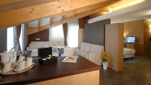 Ein modernes Hotelzimmer mit Holzboden, einer Couch, einem Fernseher und einer Essecke mit Tisch und Stühlen.