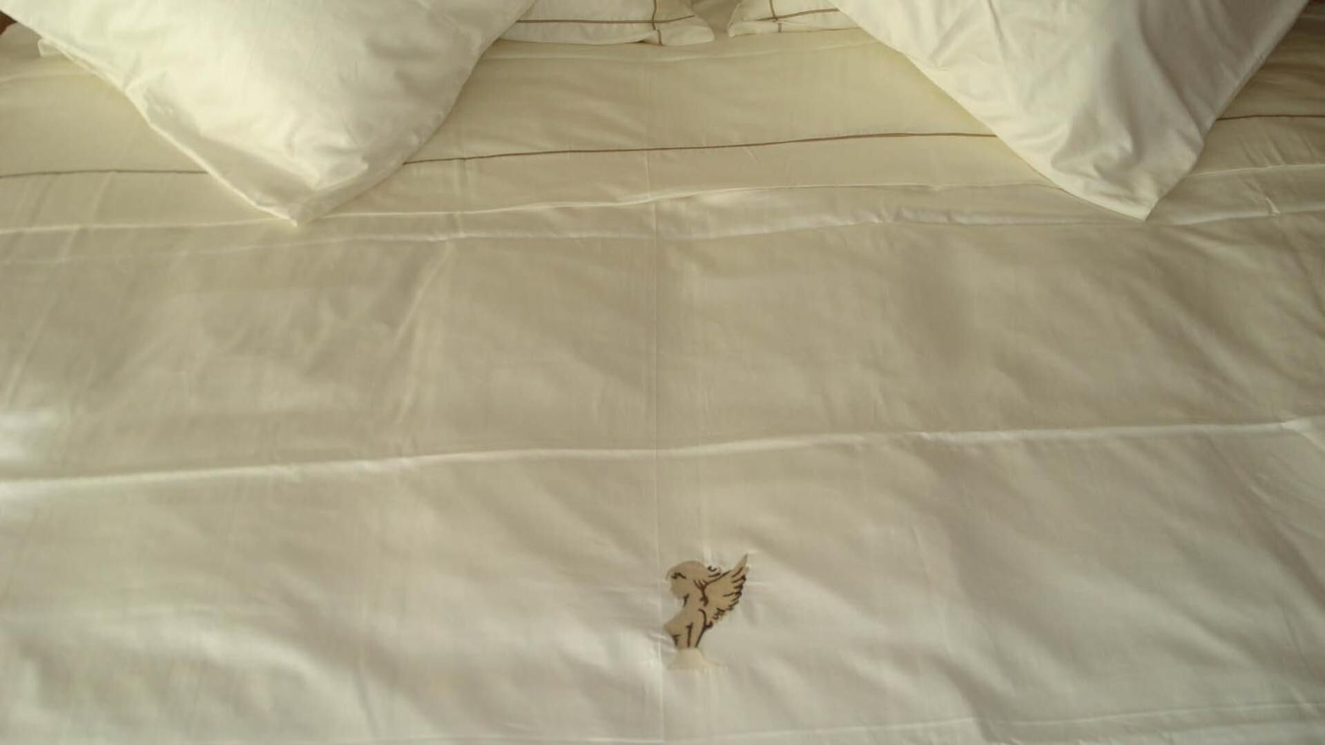 A bed with white bedding and a decorative angel embroidery.