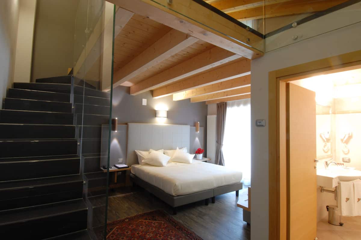 Une chambre à coucher avec un lit, une table de chevet, une lampe, un plafond en bois et un escalier.