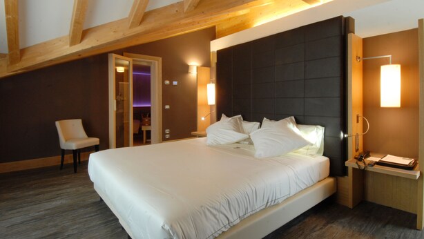 Ein Hotelzimmer mit einem großen Bett, Holzbalkendecke und einem Nachttisch mit Lampe.