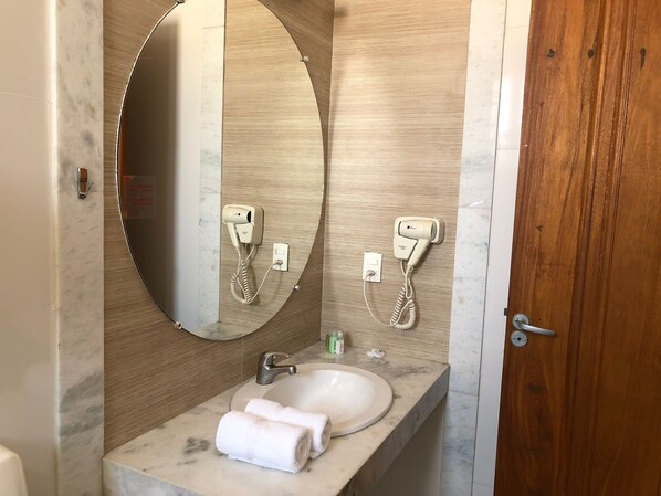 A bathroom with a marble sink, a round mirror, and two hair dryers mounted on the wall.
