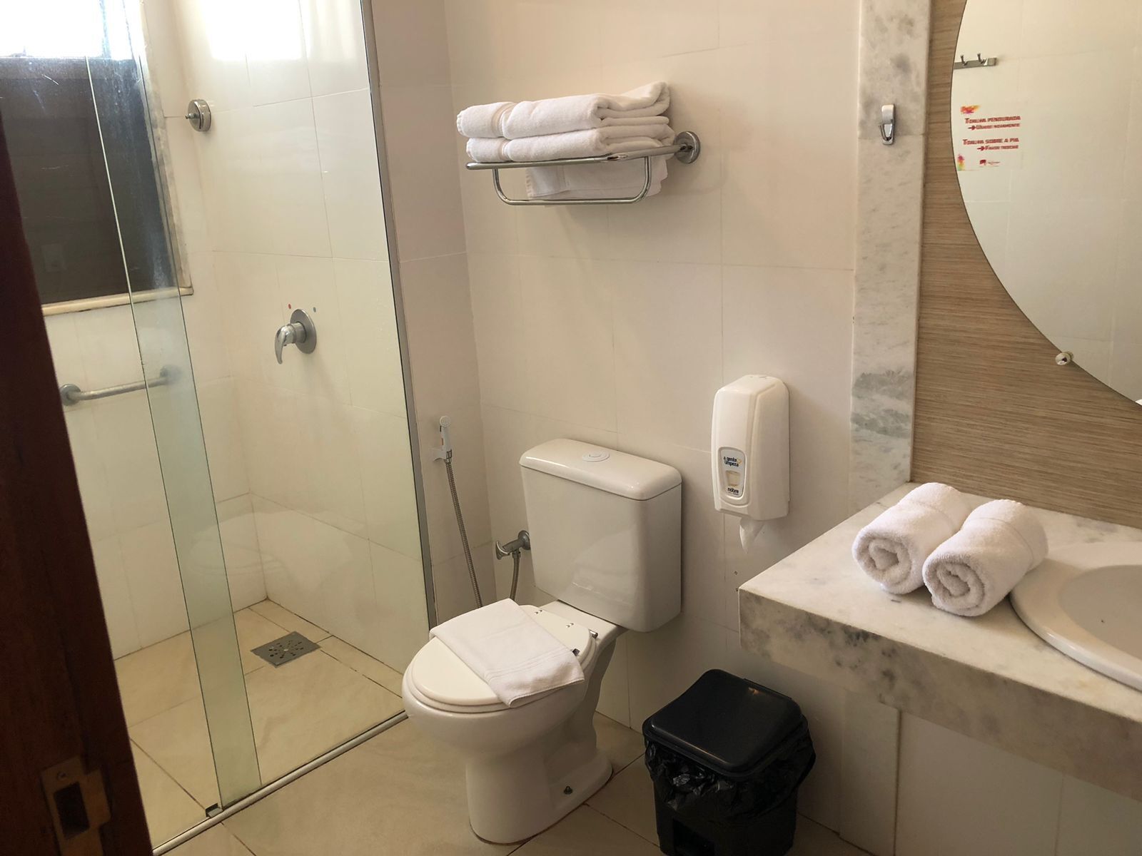 A bathroom with a glass-enclosed shower, a toilet, a hand dryer, and a sink with a towel rack.