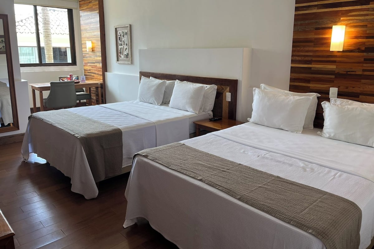 A hotel room with two beds, a desk, and a chair.