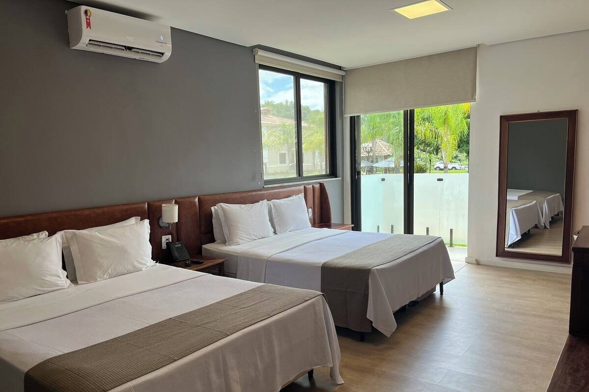 A hotel room with two beds, a large window, and a view of the outdoors.