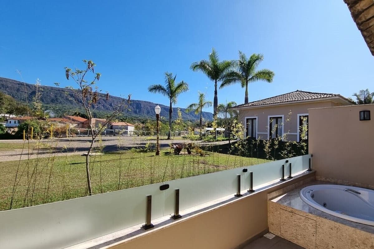 A balcony with a view of a landscaped garden, a swimming pool, and a mountain in the background.
