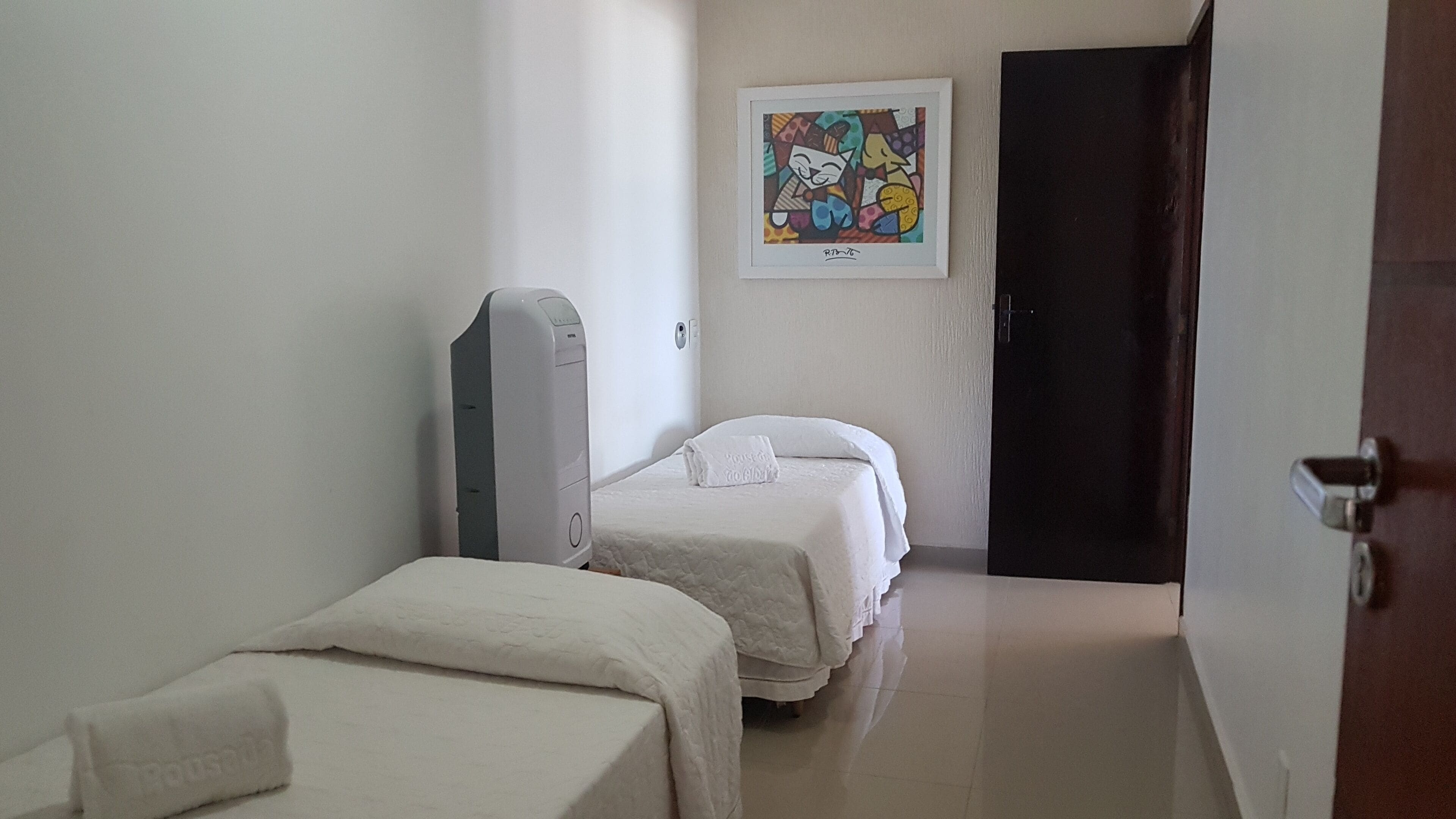 Habitación de hotel con dos camas, una puerta, una obra de arte colgada en la pared y una mesita de noche.