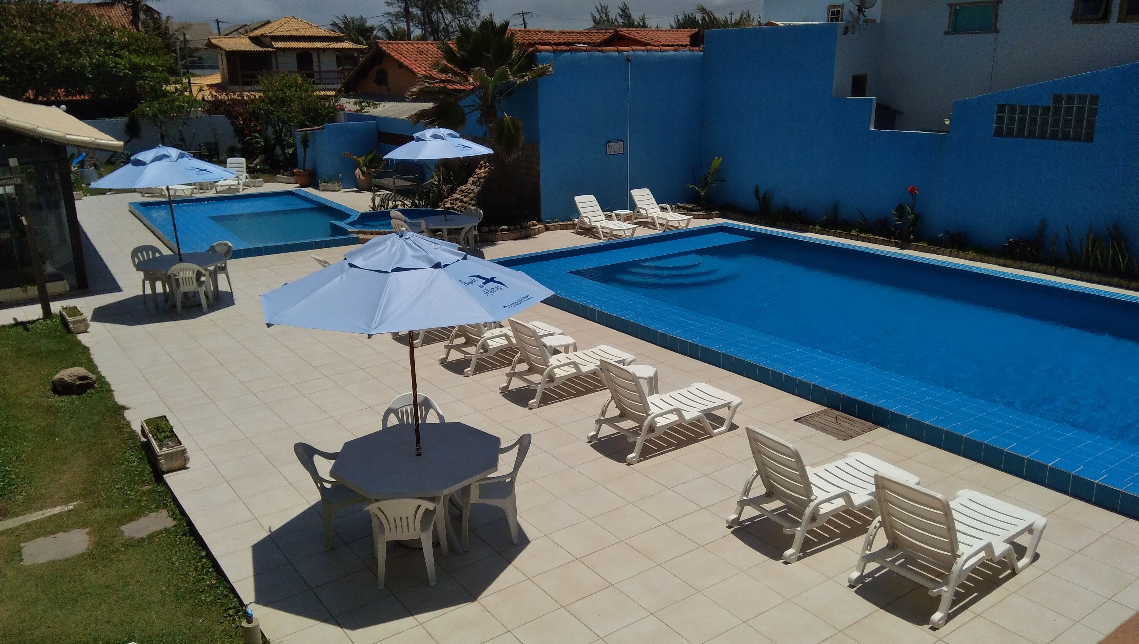 A swimming pool area with lounge chairs and umbrellas, surrounded by a blue wall and tiled flooring.