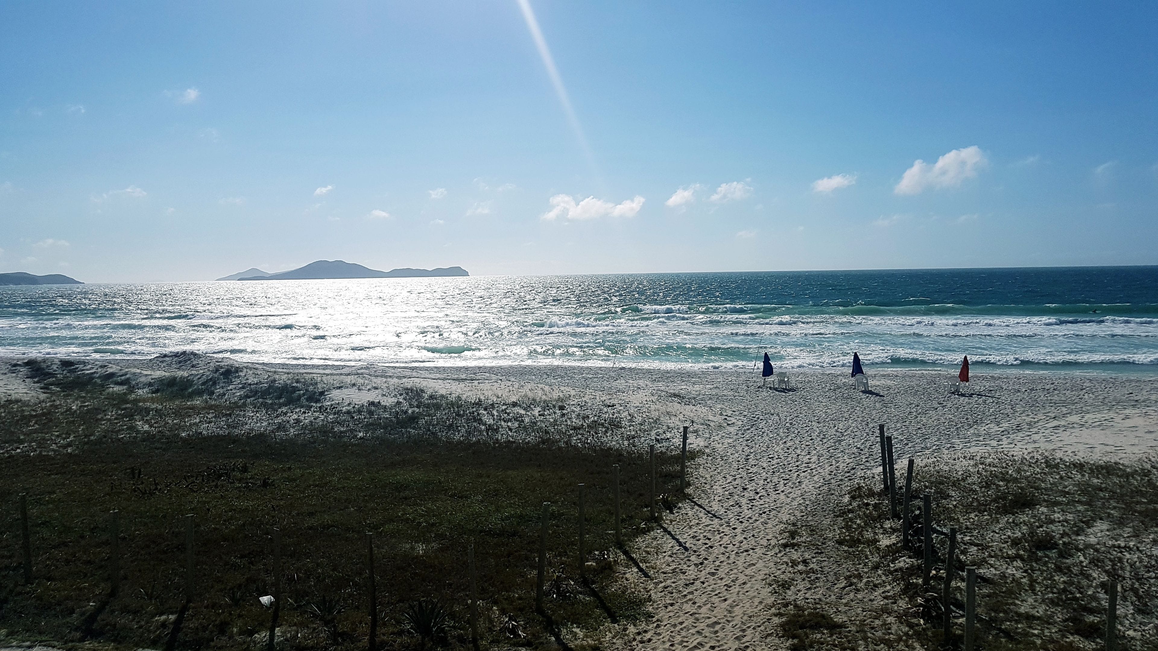 A beach with a clear sky, waves, and distant mountains.