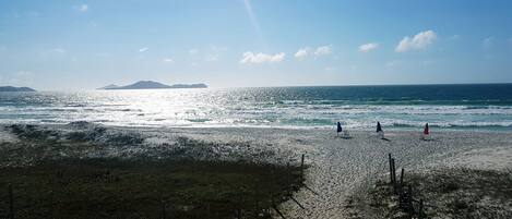 A beach with a clear sky, waves, and distant mountains.
