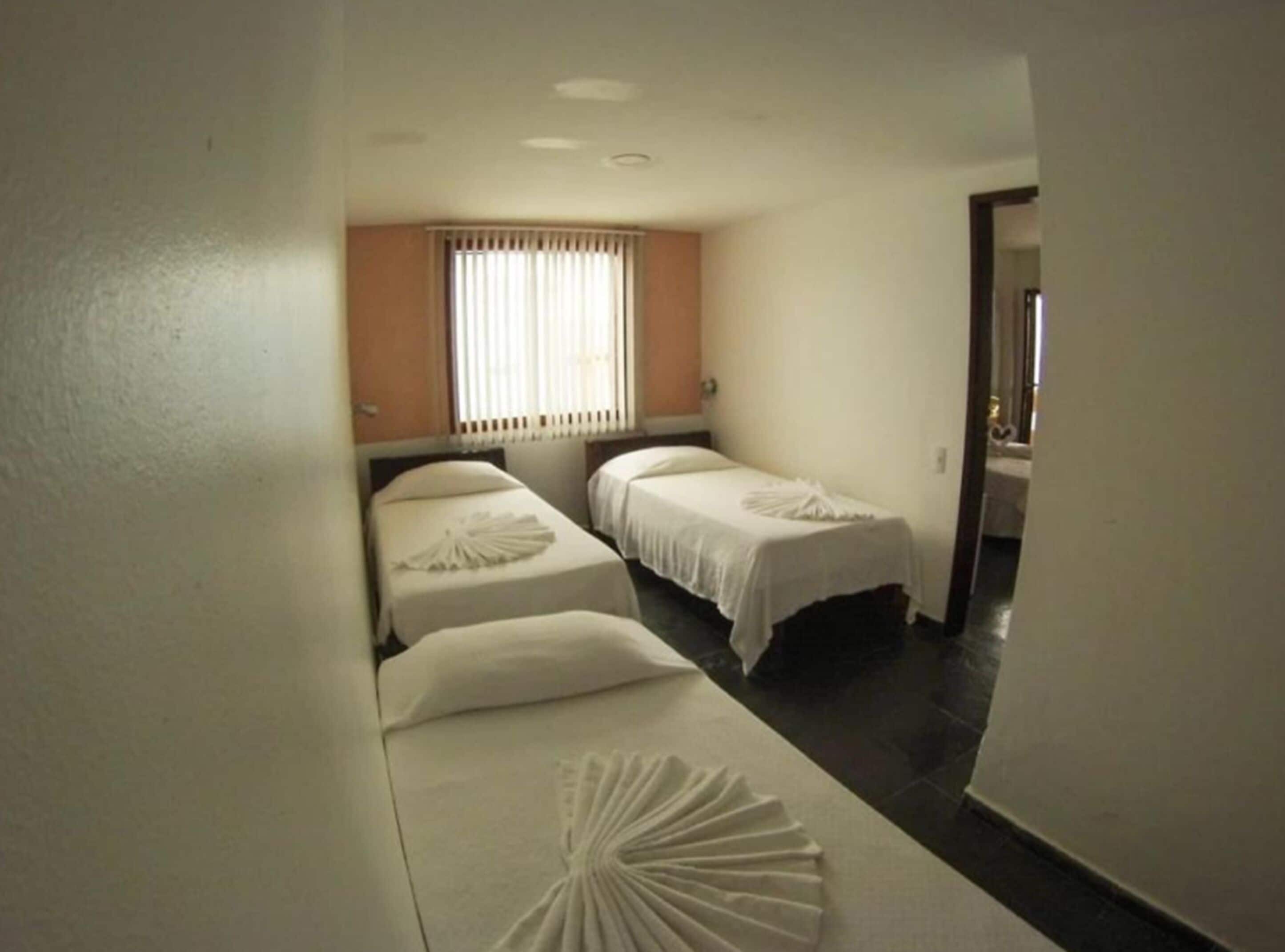A hotel room with two single beds, a window with blinds, and a door leading to another room.