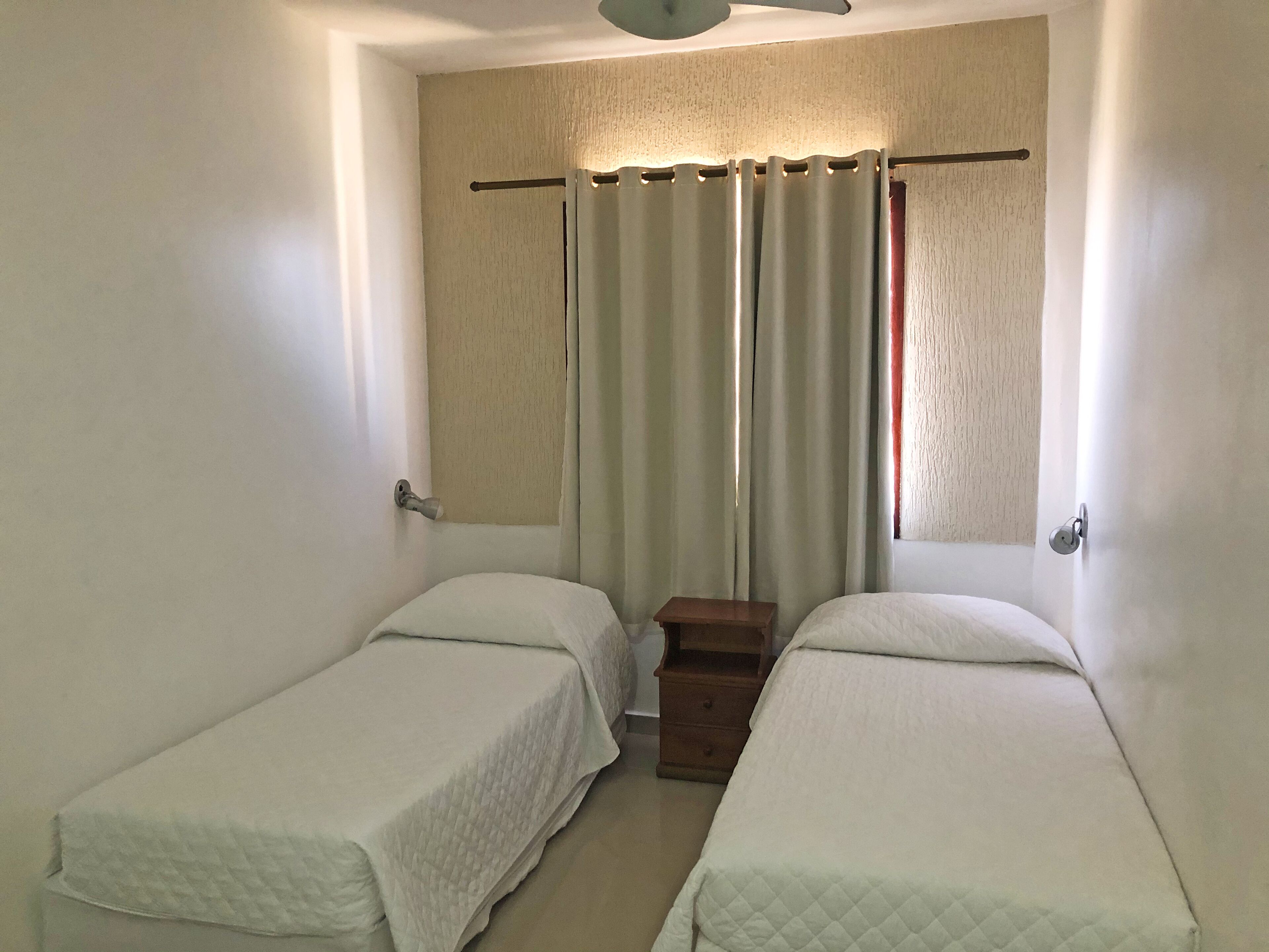 A small, clean room with two single beds, a wooden nightstand, and a curtain.