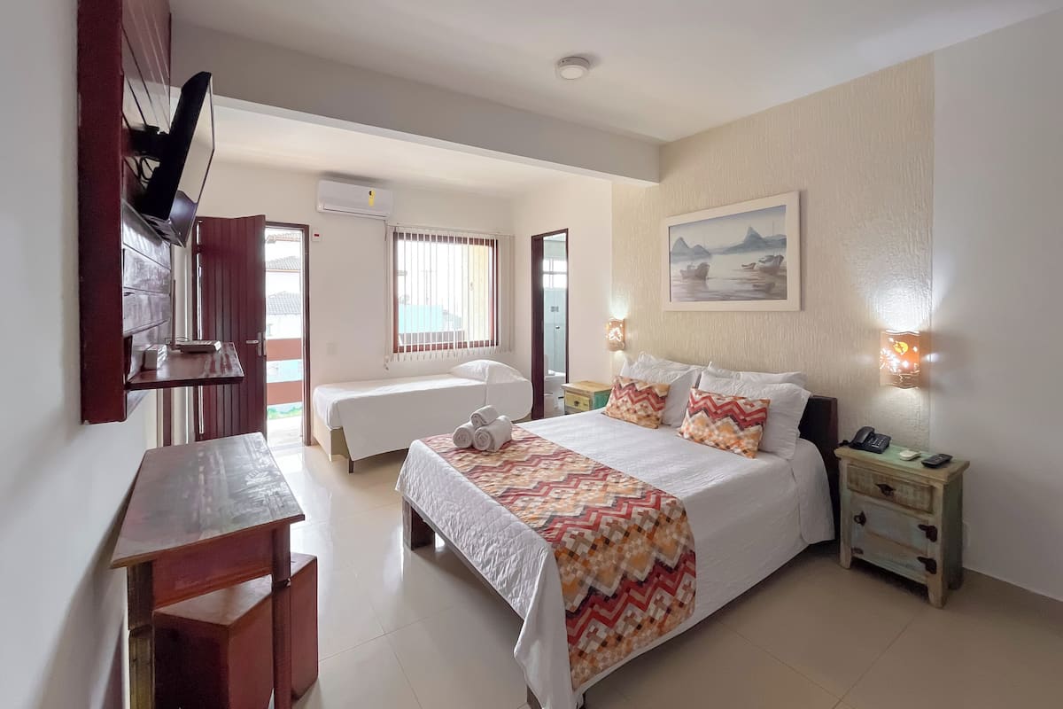 A hotel room with a bed, bedside table, desk, and a painting on the wall.
