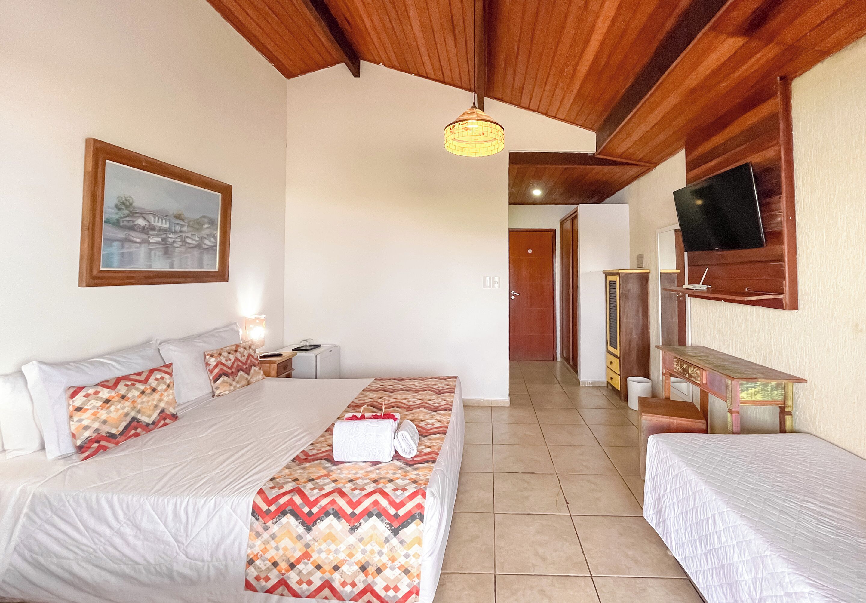 Habitación de hotel con dos camas, un televisor montado en la pared y un cuadro colgado.