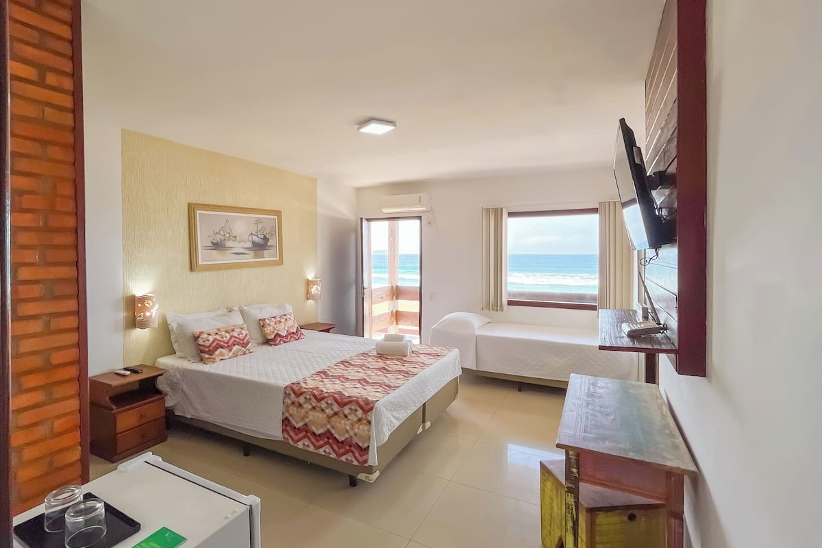 A hotel room with a bed, a desk, a TV, and a view of the ocean.