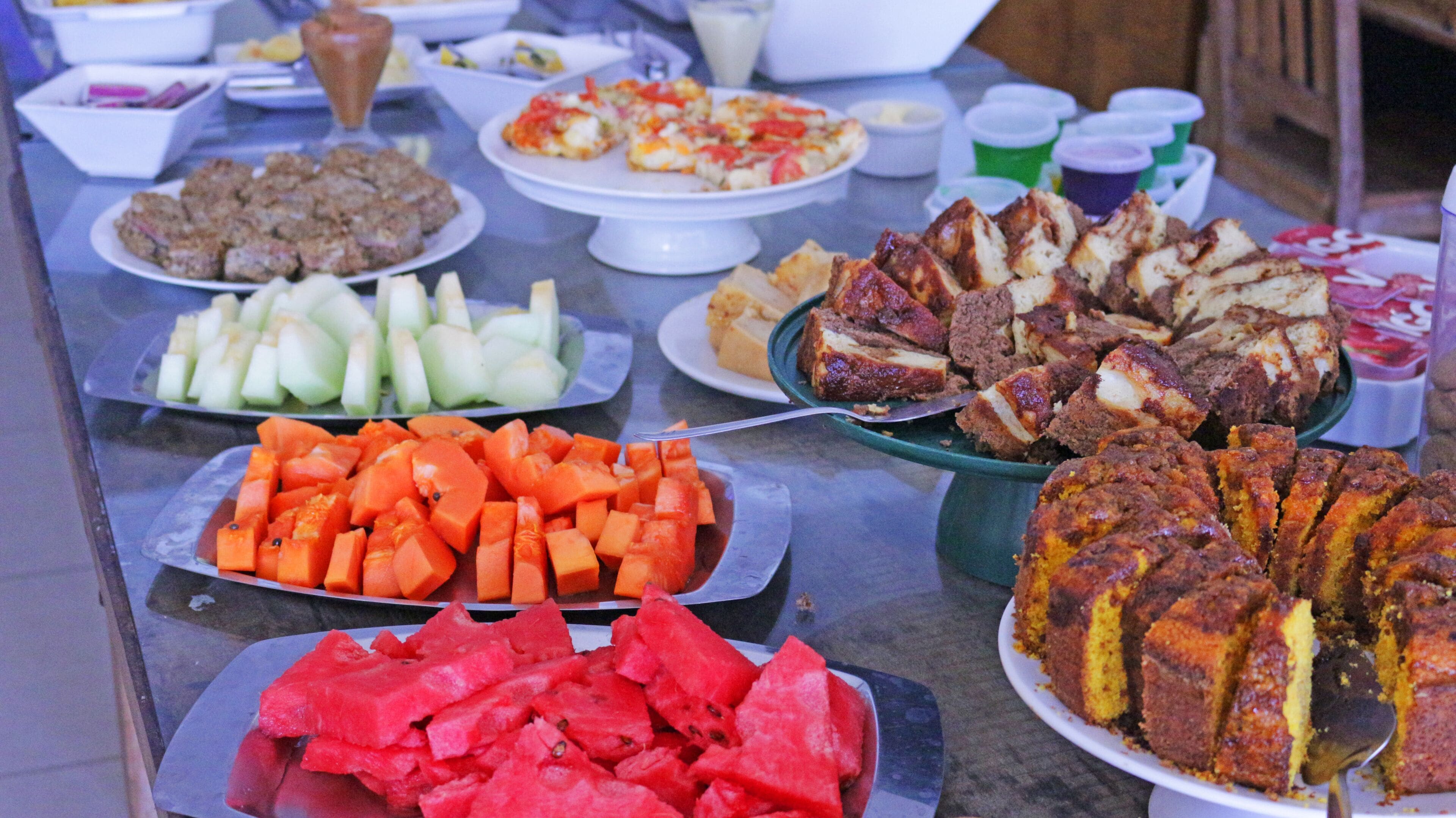 A buffet table with various dishes including sliced watermelon, carrots, and a variety of meats and cheeses.