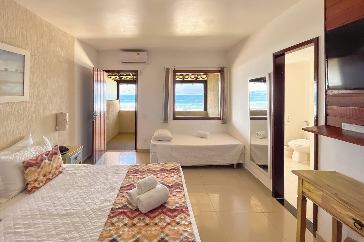 A hotel room with a bed, a small sitting area, a bathroom, and a view of the sea.