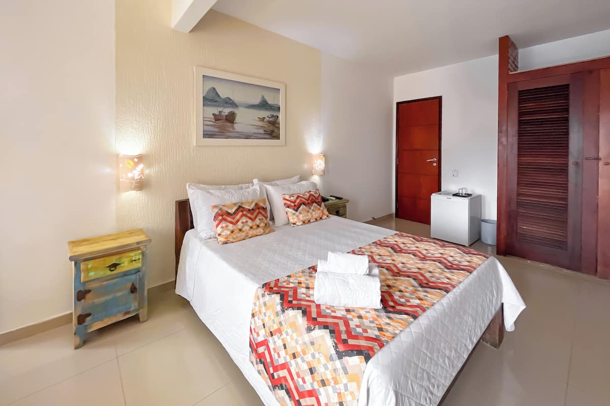 A neatly arranged bedroom with a bed, bedside tables, a painting, a wardrobe, and a small desk with a chair.