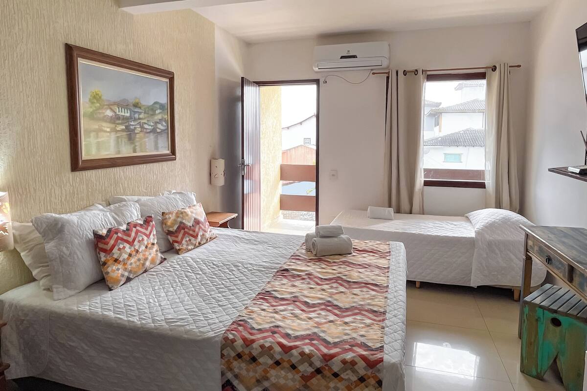 A hotel room with a large bed, a smaller bed, a painting on the wall, and an air conditioning unit.