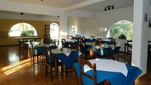 Comedor con mesas cubiertas de manteles azules y sillas de madera, ventanas amplias con arcos y piso de baldosas.