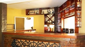 Zona de bar con mostrador de ladrillo, estantes con botellas y una barandilla metálica decorativa.