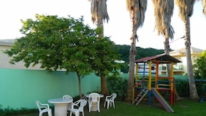 Un patio con una mesa redonda y sillas, una pequeña estructura de juegos y una pared verde.
