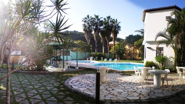 Un área de piscina con un patio de piedra, sillas de descanso y palmeras.