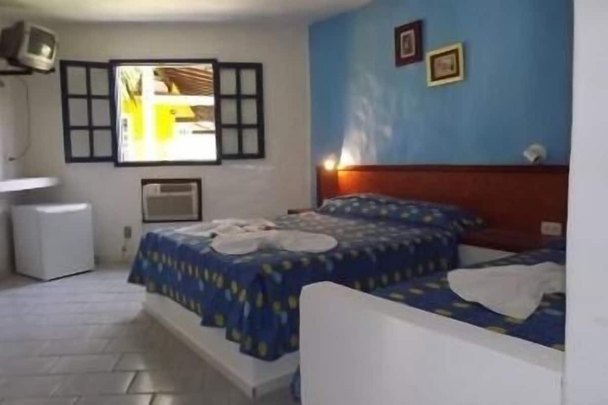 Quarto com duas camas, uma janela com persianas, mesa de cabeceira, televisão na parede e um pequeno ar condicionado.