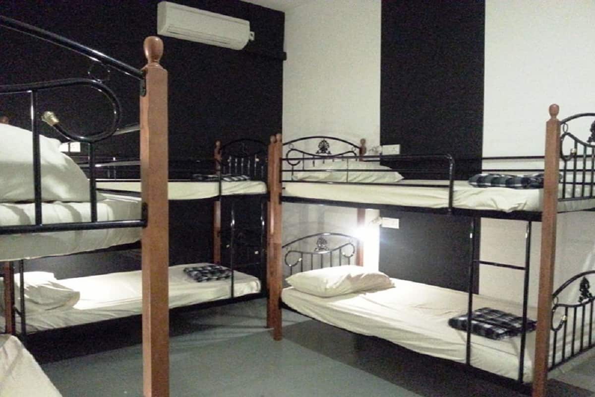 A dormitory-style room with bunk beds, a wooden headboard, and a white wall with a black panel.
